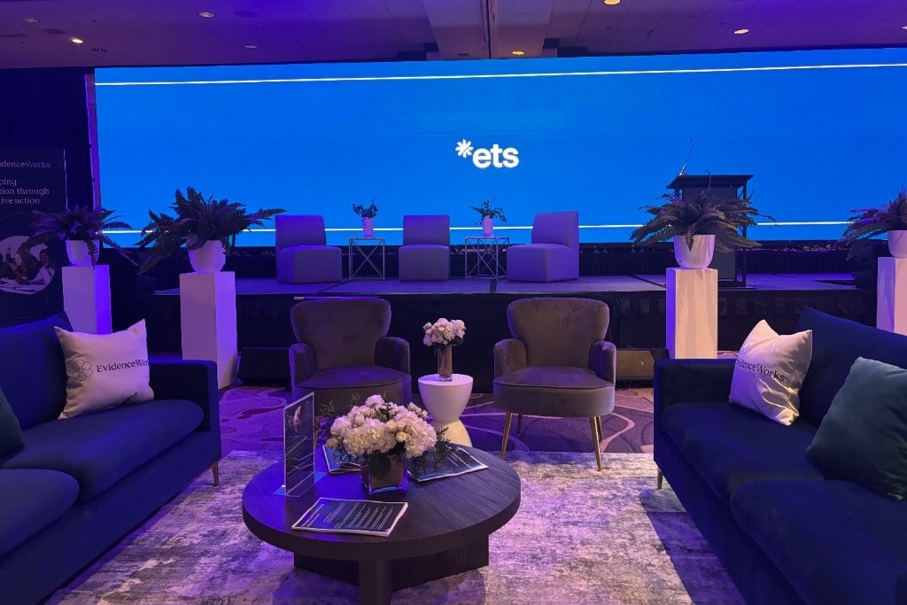 Executive lounge seating with navy sofas, accent chairs, and floral styling facing a branded stage