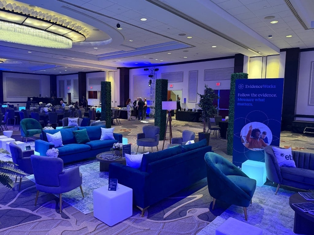 ETS National Forum hospitality lounge with navy sofas, branded pillows, and LED cube accents ETS National Forum hospitality lounge with navy sofas, branded pillows, and LED cube accents
