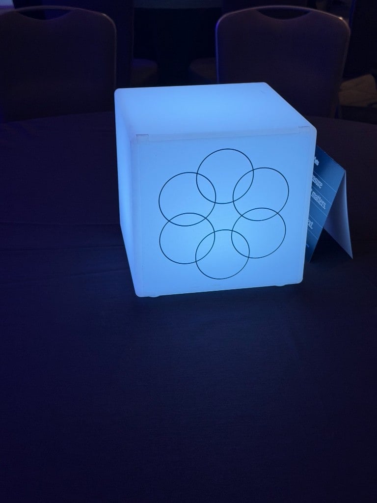 Illuminated branded cube centerpiece with interlocking circle logo on a dining table Illuminated branded cube centerpiece with interlocking circle logo on a dining table