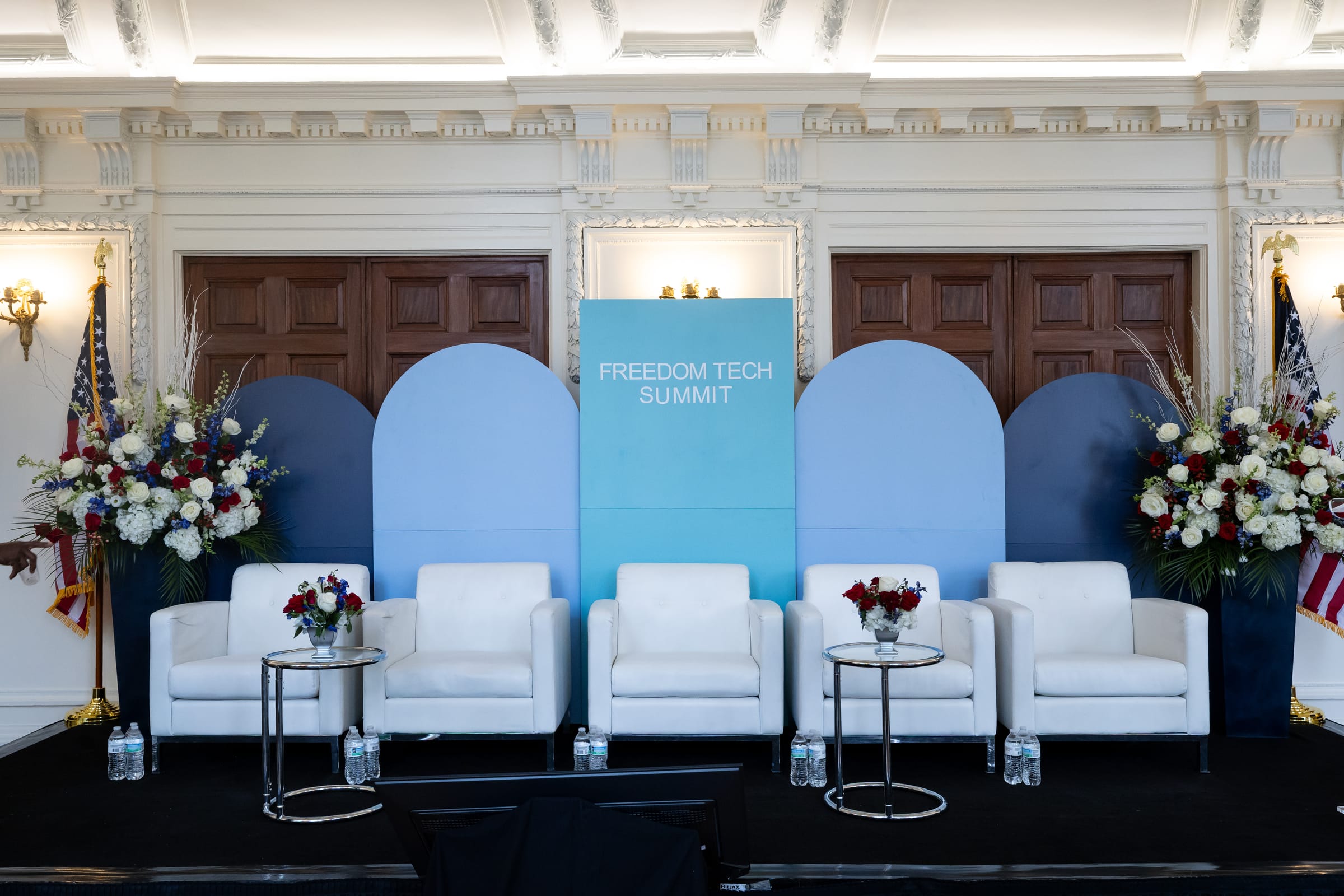 Freedom Tech Summit custom scenic backdrop and stage Custom arched scenic backdrop with Freedom Tech Summit branding, white lounge chairs, flags, and red, white, and blue florals